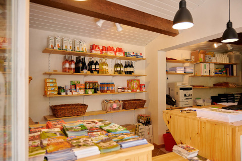 Tienda con estantes de productos y folletos en Camping La Garenne, parque vacacional en Auvernia-Ródano-Alpes, Francia.