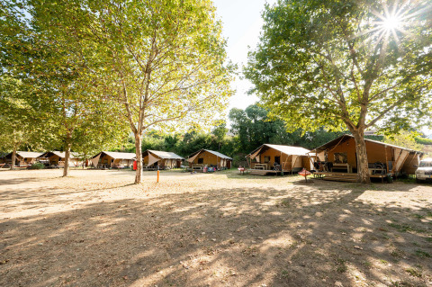 Safari tents at Camping La Garenne in Auvergne-Rhône-Alpes, France, set under leafy trees in sunlight.