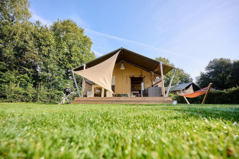 Tienda safari Villatent Nomad con terraza y hamaca en Camping de Papillon, Países Bajos, en un día soleado.