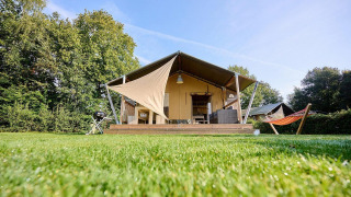 Tienda safari Villatent Nomad con terraza y hamaca en Camping de Papillon, Países Bajos, en un día soleado.