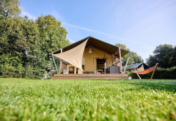 Safaritent Villatent Nomad met terras en hangmat bij Camping de Papillon in Nederland op een zonnige dag.