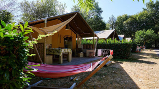 Tienda safari Villatent Nomad en Camping Domaine du Logis, Francia, con porche y hamaca en un entorno natural.