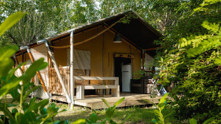 Safaritent Villatent Nomad op Camping La Chiocciola in Italië, verscholen tussen bomen en groen struikgewas.