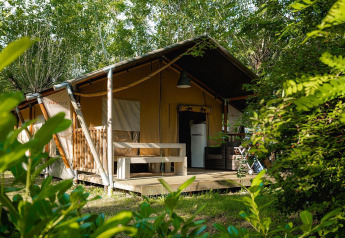 Tienda safari Villatent Nomad en Camping La Chiocciola, Italia, rodeada de vegetación y árboles verdes.