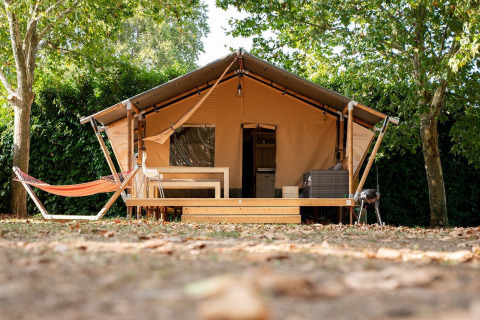 Tienda safari Villatent Nomad en Camping La Garenne en Francia, con hamaca y terraza sombreada de madera.