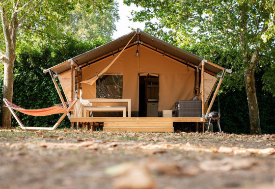 Tienda safari Villatent Nomad en Camping La Garenne en Francia, con hamaca y terraza sombreada de madera.