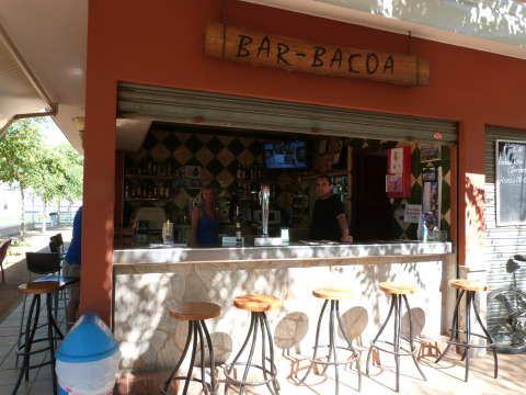 Bar al aire libre en Camping La Masia, parque vacacional en Cataluña, España, con visitantes y camarero.