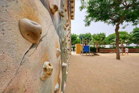 Mur d'escalade et aire de jeux à Camping La Masia, parc de vacances en Catalogne, Espagne, sous des arbres.