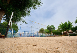 Udendørs sandvolleyballbane med net, omgivet af træer, set fra et lavt perspektiv i Camping La Masia.