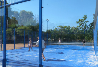 Mensen spelen padel op een blauwe buitenbaan met glazen wanden bij Camping La Masia in Catalonië, Spanje.