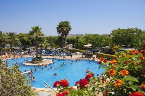 Piscina affollata di turisti e palme al campeggio La Masia, parco vacanze in Catalogna, Spagna.
