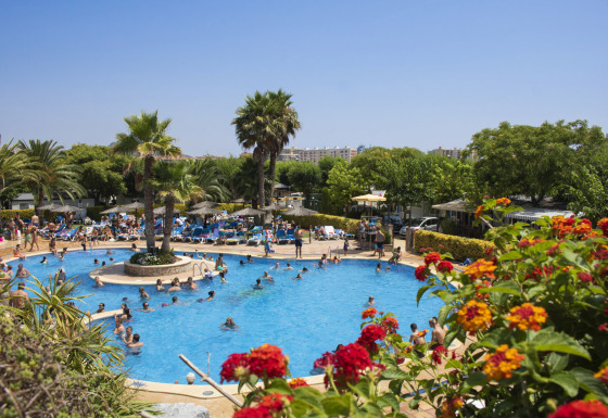 Buitenzwembad vol vakantiegangers en palmbomen bij Camping La Masia, vakantiepark in Catalonië, Spanje.
