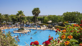Piscina affollata di turisti e palme al campeggio La Masia, parco vacanze in Catalogna, Spagna.