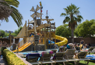 Kinderen spelen op een piratenwaterglijbaan met palmbomen bij Camping La Masia, Catalonië, Spanje.