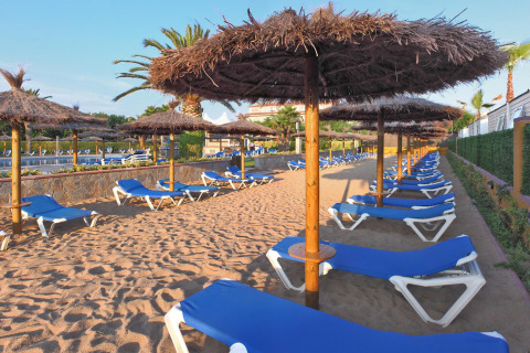 Area sabbiosa vuota con lettini blu e ombrelloni di paglia al Camping La Masia in Catalogna, Spagna.