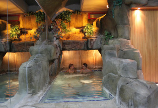 Indendørs pool med kunstige klipper og planter i Camping La Masia, Catalonien, Spanien, med to personer.