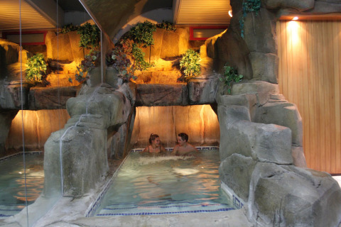 Piscina cubierta con rocas artificiales y vegetación en Camping La Masia, Cataluña, España, con dos personas.
