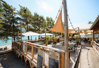 Udendørs spisested ved Camping La Presqu’île med træterrasse, parasoller og udsigt til sø i Provence.