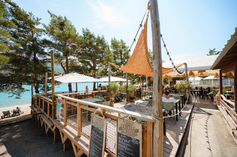 Terraza al aire libre en Camping La Presqu’île, con sombrillas y vista al lago en Provenza-Alpes-Costa Azul.