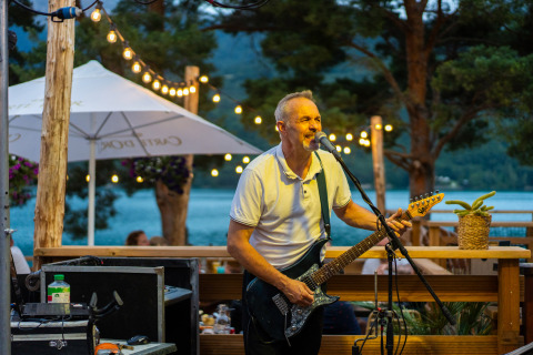 Homme jouant de la guitare électrique et chantant sur la terrasse extérieure du Camping La Presqu’île, Provence-Alpes-Côte d’Azur.