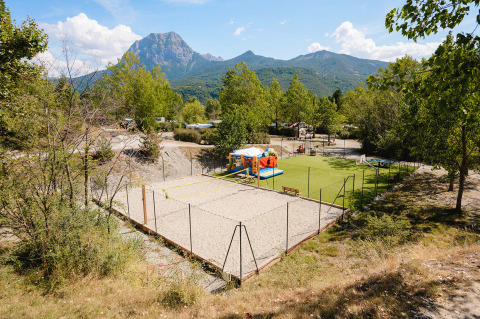 View of Camping La Presqu’île in Provence-Alpes-Côte d’Azur, France, featuring a play area, volleyball court, and mountains.