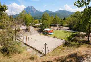 Zicht op Camping La Presqu’île in Provence-Alpes-Côte d’Azur met speelzone, volleybalterrein en bergen erachter.
