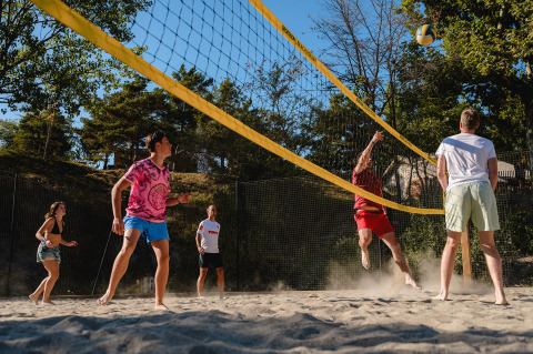 Vacacionistas juegan al vóley playa en una cancha de arena rodeada de árboles en Camping La Presqu’île, Francia.