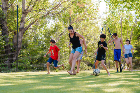 Eine Gruppe von Menschen spielt bei sonnigem Wetter Fußball auf einer Wiese im Camping La Presqu’île.