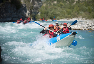 Gruppe von Menschen mit Schwimmwesten paddelt beim Wildwasser-Rafting nahe Camping La Presqu’île in Frankreich.