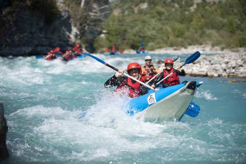 Gruppe von Menschen mit Schwimmwesten paddelt beim Wildwasser-Rafting nahe Camping La Presqu’île in Frankreich.