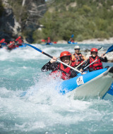 People in kayaks and safety gear rafting down a rushing river at Camping La Presqu’île in France.