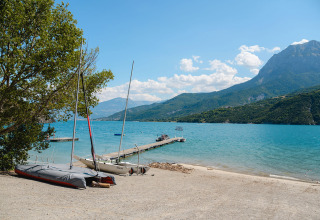 Blick auf einen See mit Badesteg, Segelbooten und Bergen im Hintergrund bei Camping La Presqu’île.