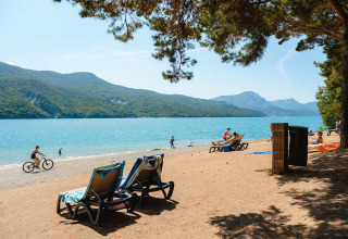Afslappende strandscene ved Camping La Presqu’île i Provence-Alpes-Côte d’Azur med udsigt over sø og bjerge.