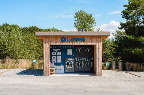 Lavanderia all'aperto in edificio di legno presso Camping La Presqu’île, Provenza-Alpi-Costa Azzurra, Francia, tra gli alberi.