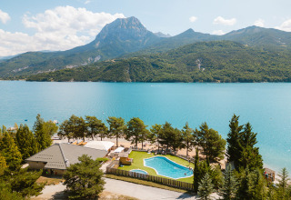 Parco vacanze con piscina vicino a un lago blu e montagne sullo sfondo in Provenza-Alpi-Costa Azzurra, Francia.