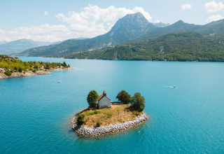 Lille ø med et hus omgivet af blåt vand i Camping La Presqu’île, Provence-Alpes-Côte d’Azur, Frankrig.