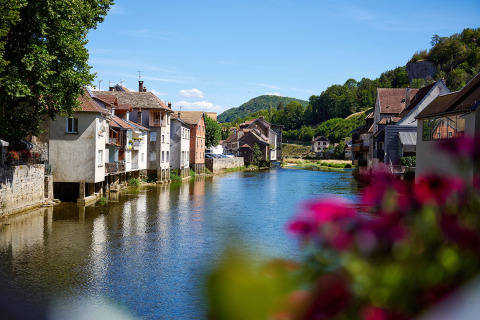 Riverside view at Camping La Roche d’Ully in Bourgogne-Franche-Comté, France, with scenic houses and flowers.