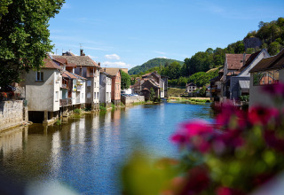 Vista sul fiume presso Camping La Roche d’Ully in Borgogna-Franca Contea, Francia, con case e fiori pittoreschi.