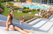 Children enjoy a waterslide with a swimming pool and grassy sunbathing area at Camping La Roche d’Ully, France.
