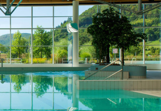 Indoor swimming pool with large windows overlooking green hills at Camping La Roche d’Ully, France.