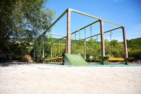 Outdoor playground obstacle course at Camping La Roche d’Ully, surrounded by trees under a clear blue sky.