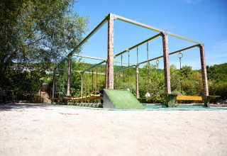 Outdoor playground obstacle course at Camping La Roche d’Ully, surrounded by trees under a clear blue sky.