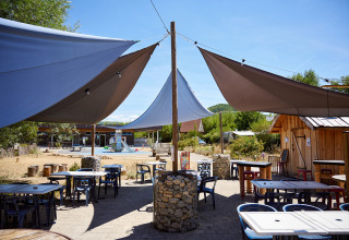 Udendørs cafeteriaområde med solsejl og borde på Camping La Roche d’Ully, Bourgogne-Franche-Comté, Frankrig.