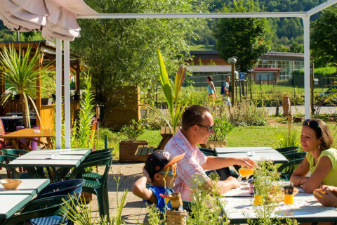 Family enjoys drinks at an outdoor table at Camping La Roche d’Ully holiday park in Bourgogne-Franche-Comté, France.