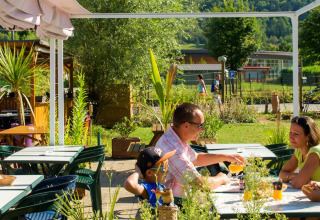Familie nyder drikkevarer og natur ved udendørs café på Camping La Roche d’Ully i Bourgogne-Franche-Comté.