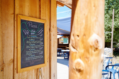 Krijtbord met pizzamenu aan een houten wand bij Camping La Roche d’Ully, Bourgogne, Frankrijk.