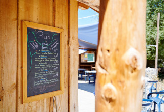 Krijtbord met pizzamenu aan houten wand bij Camping La Roche d’Ully in Bourgogne, Frankrijk.