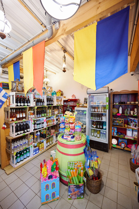 Interior view of a shop at Camping La Roche d’Ully with colorful flags, toys, and shelves of groceries.