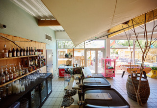 Bar intérieur du Camping La Roche d’Ully avec boissons, jeux et vue sur la terrasse extérieure ensoleillée.