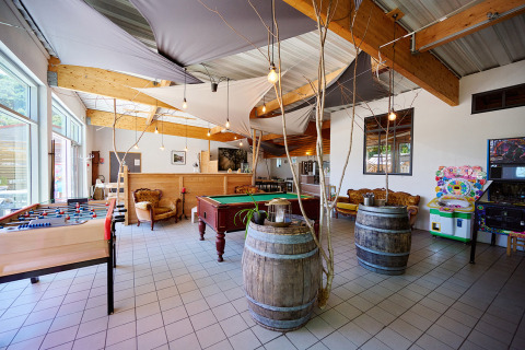 Indoor recreation room at Camping La Roche d’Ully with pool table, foosball, cozy seating and arcade games.
